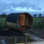 Barrel garden sauna 280 front view with interior lighting at dusk