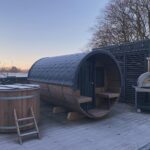 Barrel sauna 330 with balcony installed outdoors next to cold tub