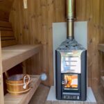 Wood-fired sauna heater burning inside barrel sauna 330 with balcony