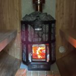 Wood-fired sauna heater with visible flames inside barrel sauna 330 with balcony
